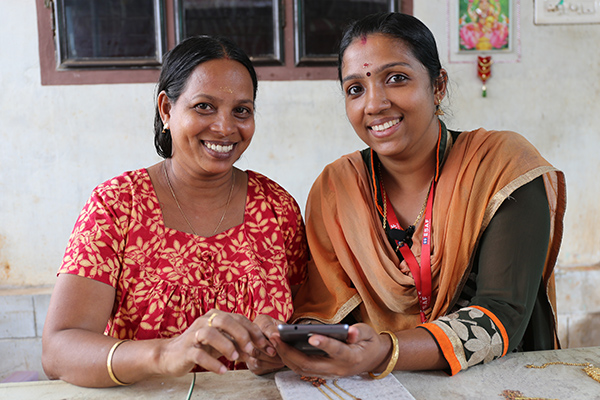 A loan officer helps a woman process her small loan with the help of a tablet in India.