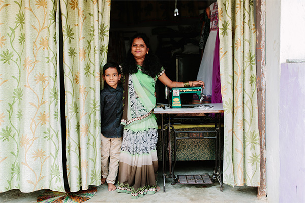 An Indian mother and her son stand in the doorway of a small shop with her sewing machine.