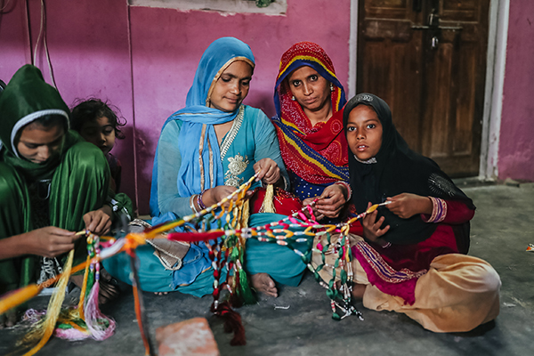 Women sit together and make traditional armbands in India.