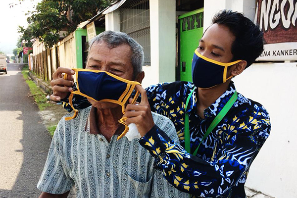 A loan officer in Indonesia helps an elderly man put on his mask